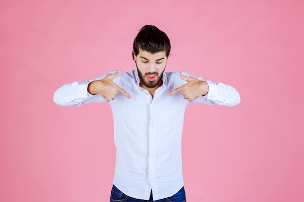 Hombre con camisa blanca apuntando a sí mismo.