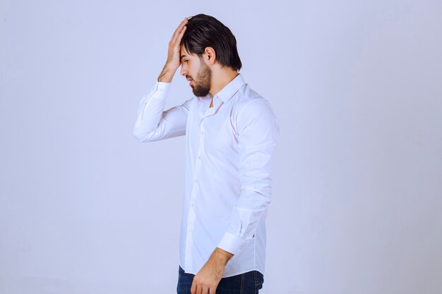 Hombre con camisa blanca cubriéndose la cara, se siente triste y tiene dolor de cabeza.