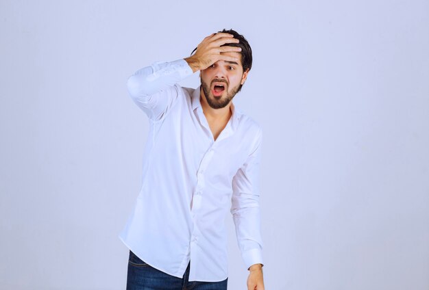 Hombre con camisa blanca cubriéndose la cara, se siente triste y tiene dolor de cabeza.