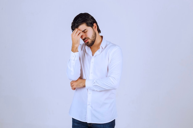 Hombre con camisa blanca cubriéndose la cara, se siente triste y tiene dolor de cabeza.