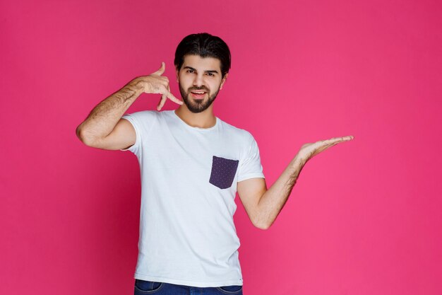 Hombre con camisa blanca haciendo distintivo de llamada y pidiendo llamar.