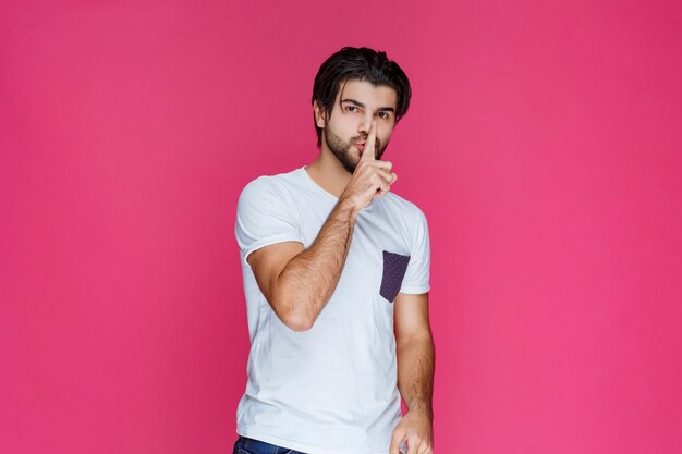 Hombre con camisa blanca haciendo señal de silencio.