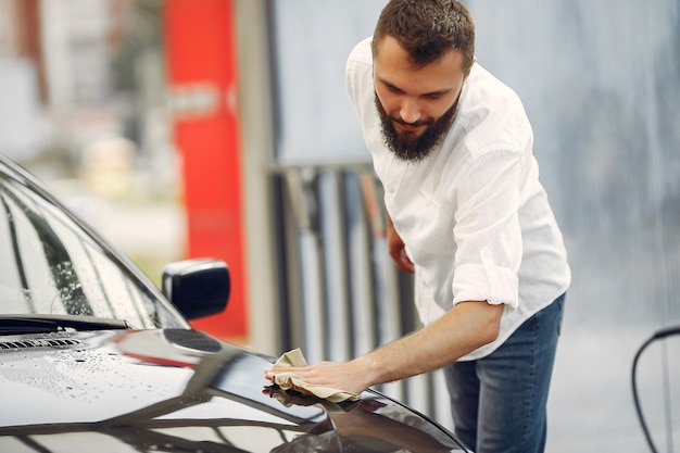 El hombre con una camisa blanca limpia un automóvil en un lavadero de autos