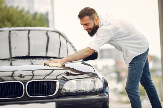 El hombre con una camisa blanca limpia un automóvil en un lavadero de autos