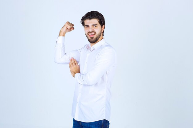 Hombre con camisa blanca mostrando los músculos del brazo y el puño.