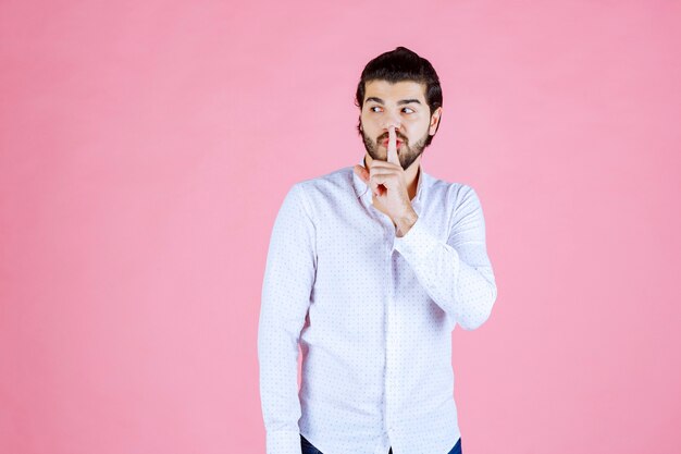 Hombre con camisa blanca pidiendo silencio.