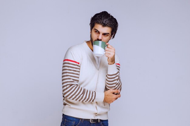 Hombre de camisa blanca sosteniendo y posando con una taza de café.