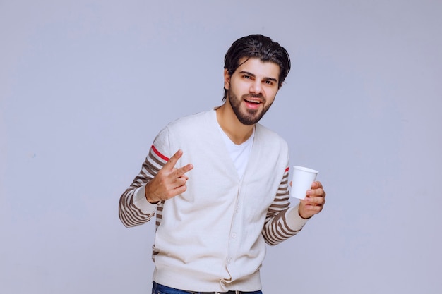 Hombre con camisa blanca sosteniendo una taza de café y apuntando a ella.