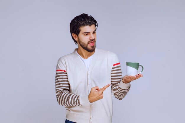 Hombre con camisa blanca sosteniendo una taza de café y apuntando a ella.