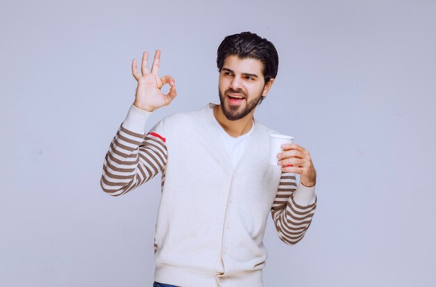 Hombre con camisa blanca sosteniendo una taza de café desechable.