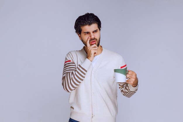 Hombre con camisa blanca sosteniendo una taza de café y parece pensativo.