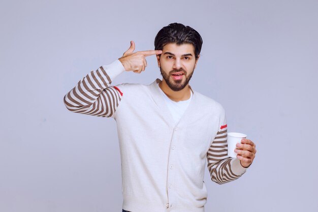 Hombre de camisa blanca sosteniendo una taza de café y pensando.