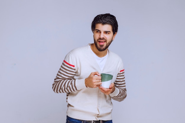 Hombre con camisa blanca sosteniendo una taza de café, tomando café y sintiéndose lleno de energía.