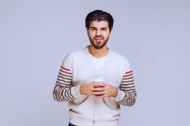 Hombre de camisa blanca sosteniendo y tomando una taza de café.