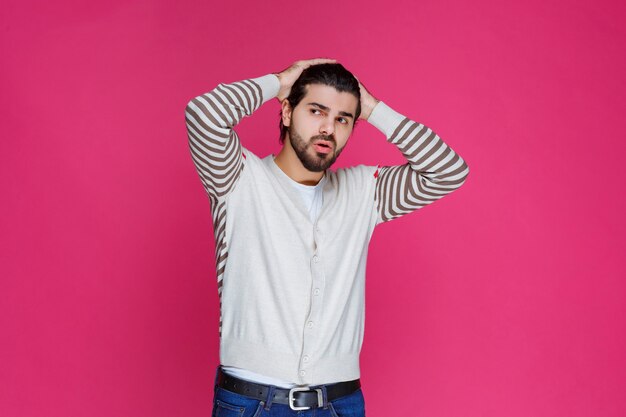 El hombre con camisa blanca tiene dolor de cabeza y se sostiene la cabeza.