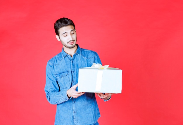 Hombre en camisa de mezclilla con caja de regalo plateada y parece confundido e inesperado.