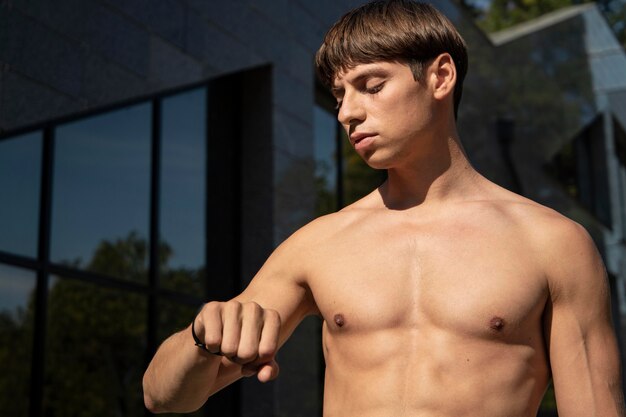 Hombre sin camisa mirando su banda de fitness mientras hace ejercicio al aire libre