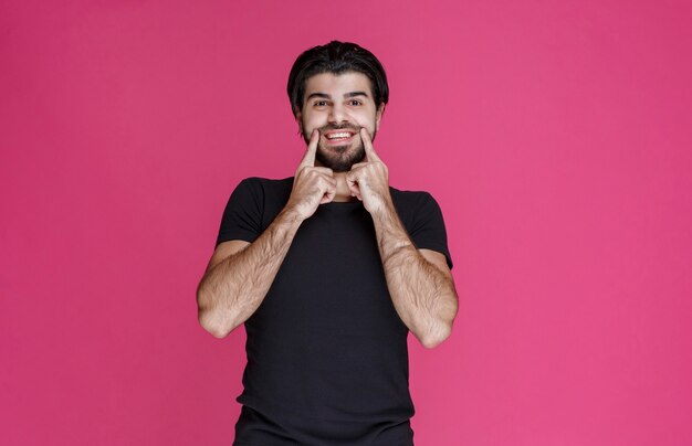 Foto gratuita hombre de camisa negra apuntando con su boca y pregunta sonriendo