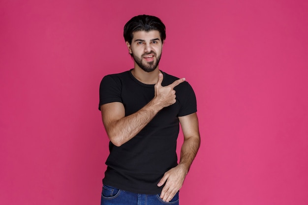 Hombre de camisa negra con barba apuntando a algo de manera confusa o mostrando la dirección