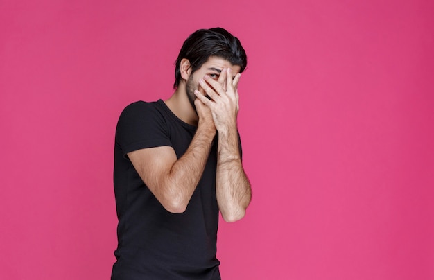 Foto gratuita hombre de camisa negra mirando a través de sus dedos