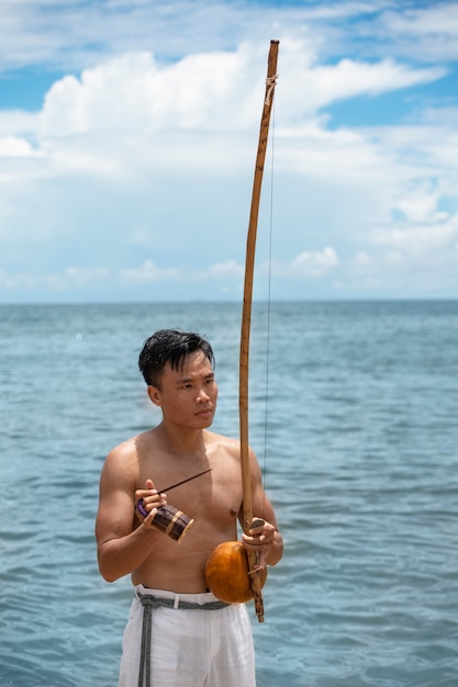 Foto gratuita hombre sin camisa practicando capoeira en la playa con arco de madera