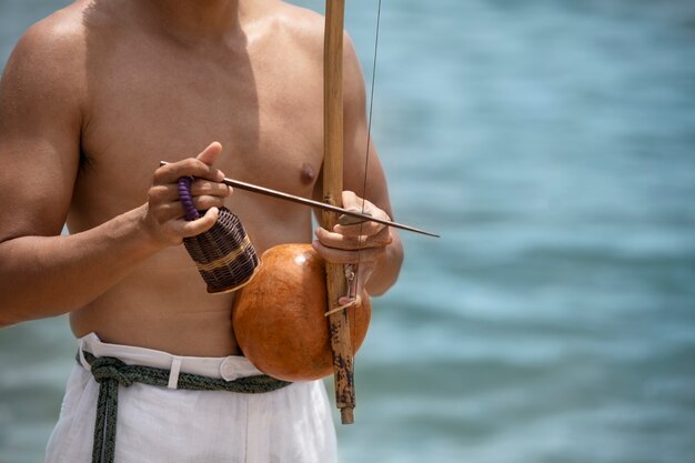 Hombre sin camisa practicando capoeira en la playa con arco de madera