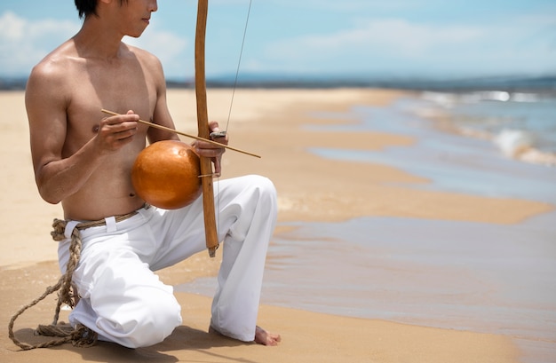Hombre sin camisa practicando capoeira en la playa con arco de madera