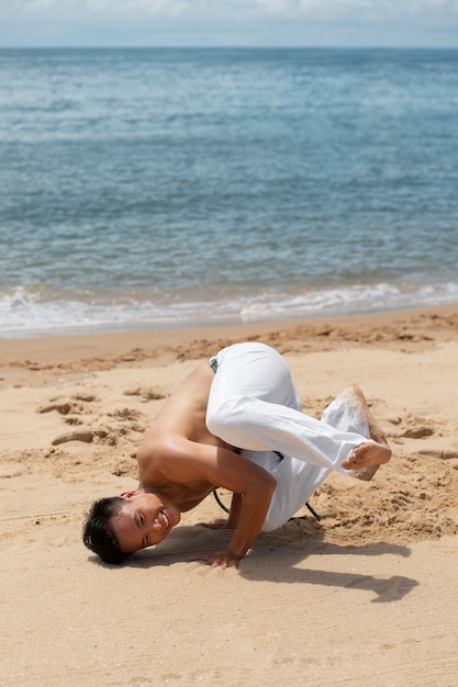 Hombre sin camisa practicando capoeira en la playa