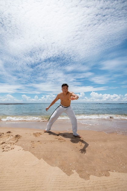 Foto gratuita hombre sin camisa practicando capoeira en la playa