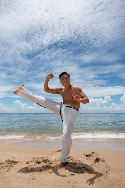 Hombre sin camisa practicando capoeira en la playa