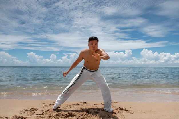 Hombre sin camisa practicando capoeira en la playa