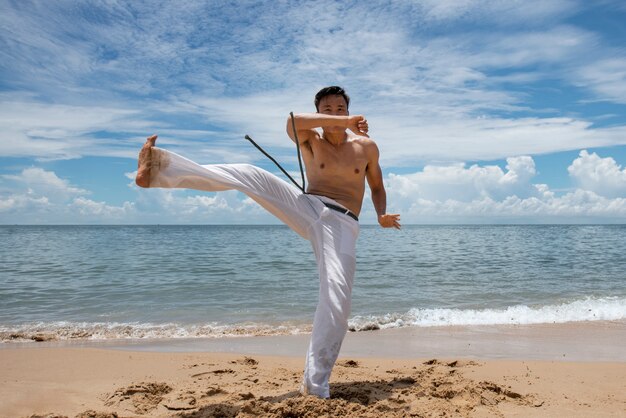 Hombre sin camisa practicando capoeira en la playa