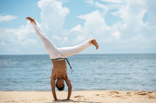 Hombre sin camisa practicando capoeira solo en la playa