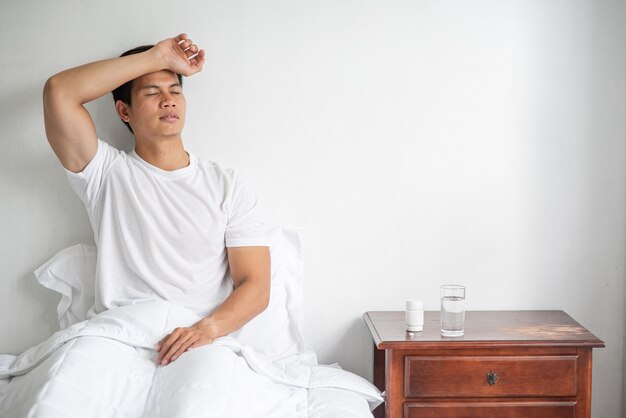 Foto gratuita el hombre de camisa a rayas estaba enfermo, sentado en la cama y con la mano en la frente.