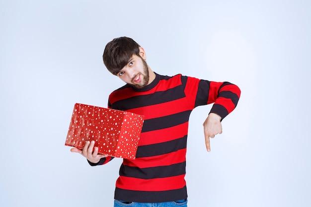 Hombre con camisa a rayas rojas con una caja de regalo roja y llamando a alguien para que se la presente.