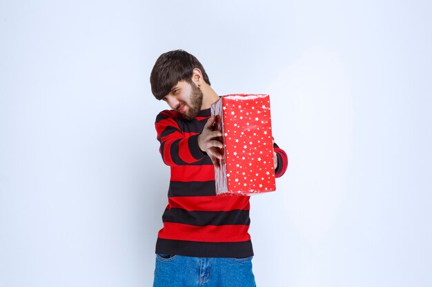 Hombre de camisa a rayas rojas con una caja de regalo roja y ofreciéndola