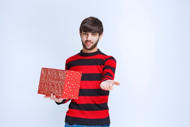 Hombre de camisa a rayas rojas con una caja de regalo roja y ofreciéndola