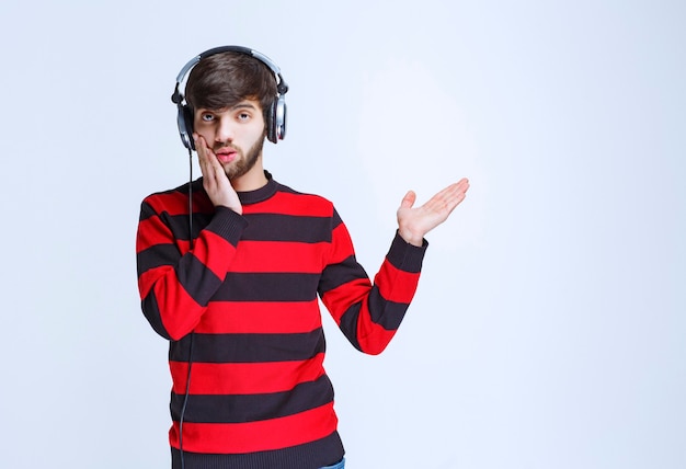 Hombre de camisa a rayas rojas escuchando auriculares y parece confundido y pensativo.