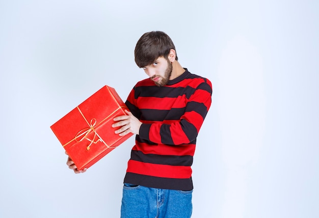 Hombre con camisa de rayas rojas sosteniendo una caja de regalo roja, entregándola y presentándola al cliente oa su novia.