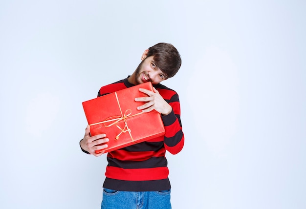 Hombre en camisa de rayas rojas sosteniendo una caja de regalo roja, entregándola y presentándola