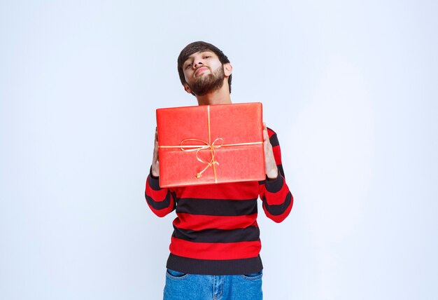 Hombre en camisa de rayas rojas sosteniendo una caja de regalo roja, entregándola y presentándola