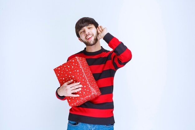 Hombre en camisa de rayas rojas sosteniendo una caja de regalo roja, entregándola y presentándola