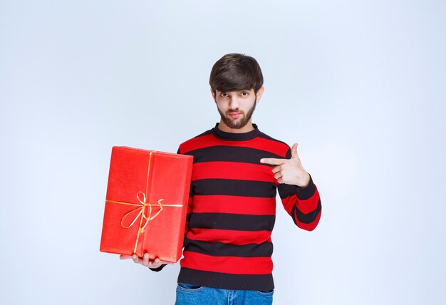 Hombre de camisa a rayas rojas sosteniendo una caja de regalo roja y promoviéndola.