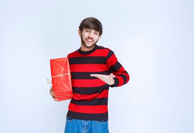 Hombre de camisa a rayas rojas sosteniendo una caja de regalo roja y promoviéndola.