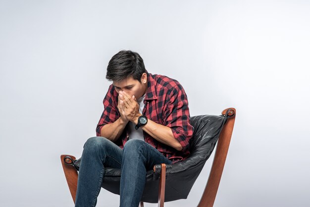 El hombre con una camisa a rayas se sienta enfermo y se sienta en una silla y se cruza de brazos.