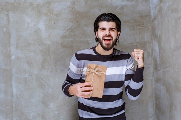 Hombre en camisa a rayas sosteniendo una caja de regalo de cartón y mostrando su puño