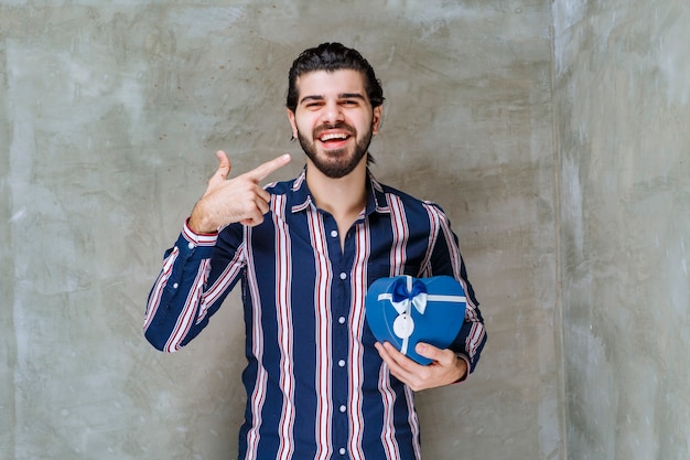 Hombre de camisa a rayas sosteniendo una caja de regalo con forma de corazón azul