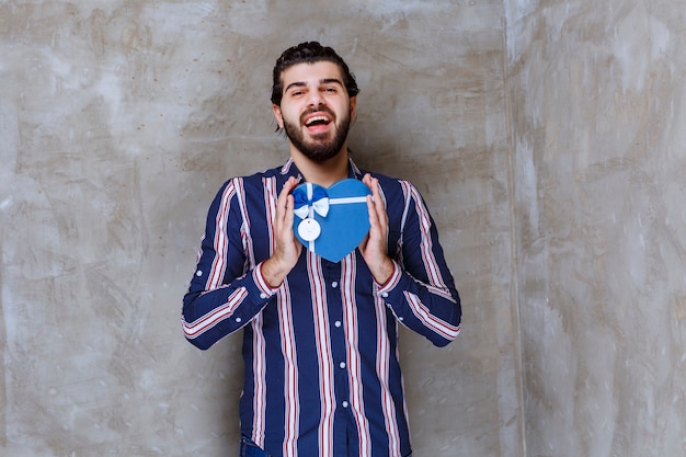 Hombre de camisa a rayas sosteniendo una caja de regalo con forma de corazón azul