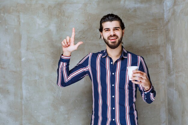 Hombre con camisa a rayas sosteniendo una taza de agua desechable blanca y pensando en cómo venderla