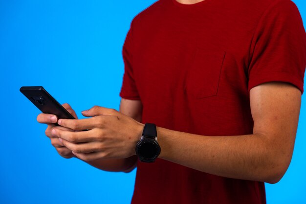 Foto gratuita hombre de camisa roja sosteniendo y charlando en un teléfono inteligente en azul.